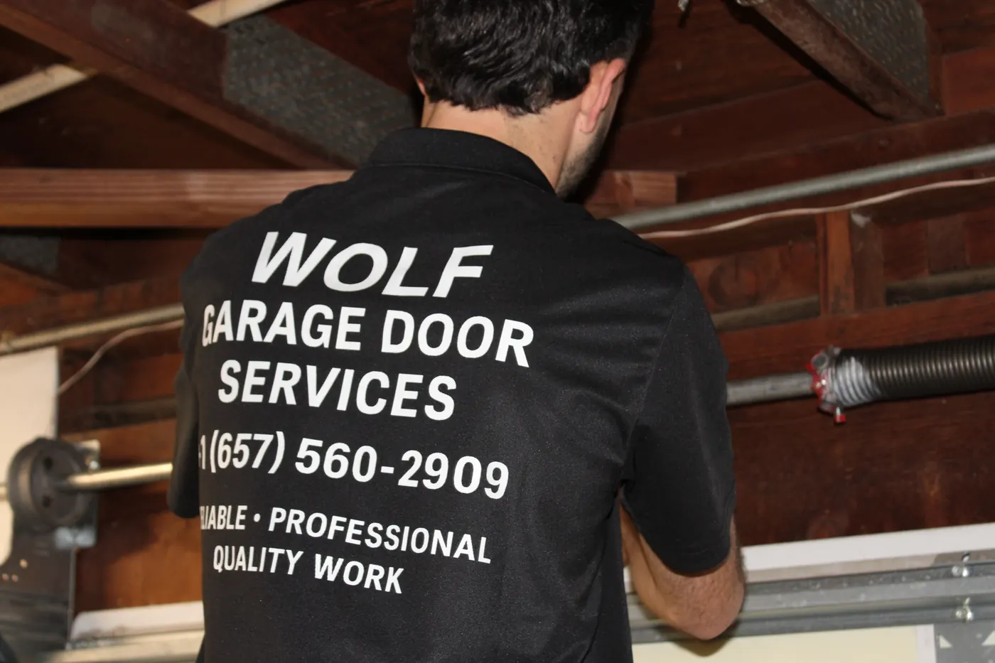 Wolf Garage Door Services technician winding a torsion spring above a garage door