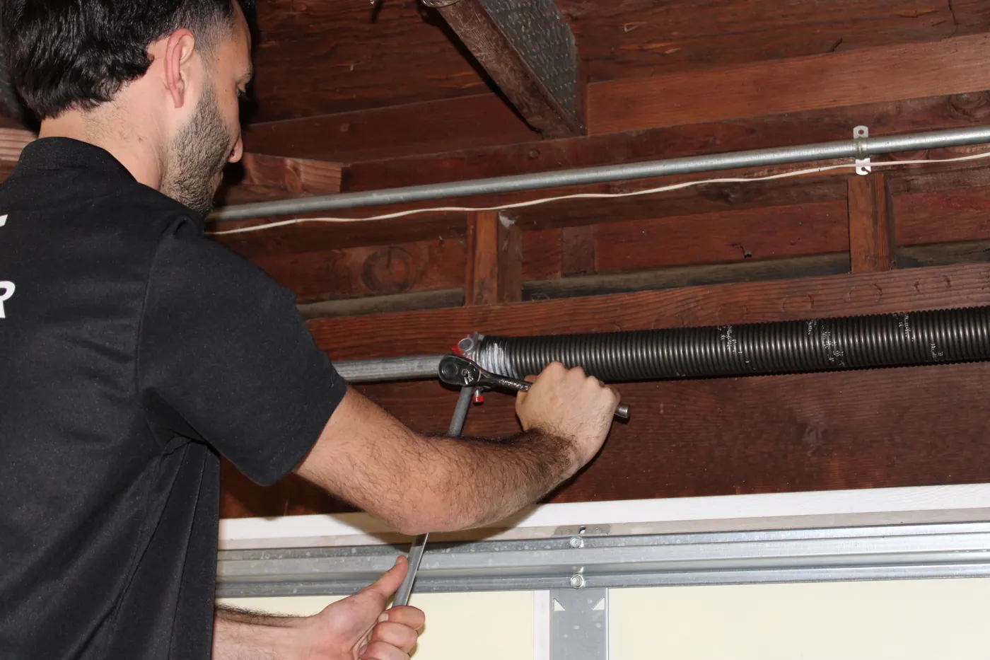 Close-up of a technician working on the torsion tube and cable drum of a garage door