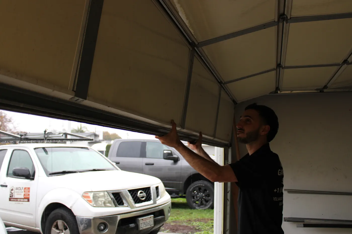 Wolf technician lifting a garage door with the company truck parked outside